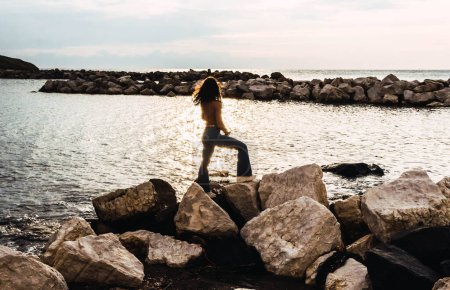 Téléchargez les photos : Woman on stones in front of the sea at sunset - en image libre de droit