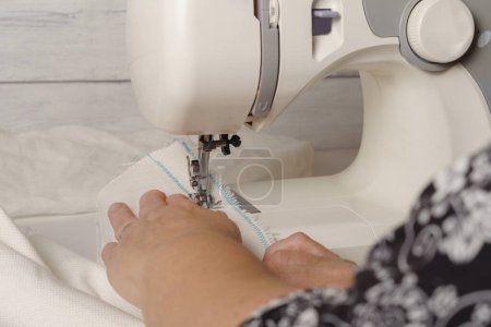 Téléchargez les photos : Close-up of woman's hands sewing a fabric with blue thread on a sewing machine - en image libre de droit