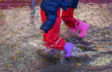 Téléchargez les photos : Two children walking through a puddle of water with their boots on a rainy day - en image libre de droit
