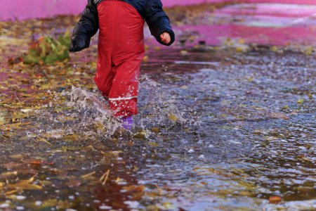 Photo for Child splashing water with boots and water pants in a puddle on a rainy day - Royalty Free Image