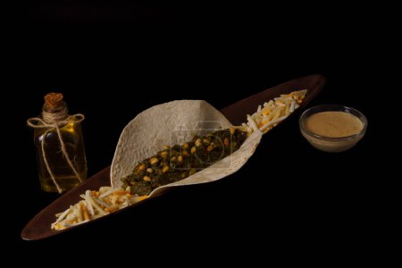 Téléchargez les photos : Taco with spinach and pine nuts bowl with cheese sauce and several types of cheese as garnish bottle of olive oil and black background - en image libre de droit