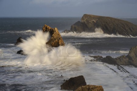 Foto de Large winter waves crash overy rocky coastline at Playa de la Arnia, Cantabria, Spain - Imagen libre de derechos