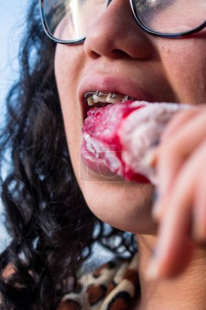 Photo for Girl with braces biting a red ice cream in summer - Royalty Free Image
