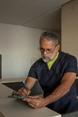 Foto de Attractive senior doctor in dark blue medical uniform writing administrative forms - Imagen libre de derechos