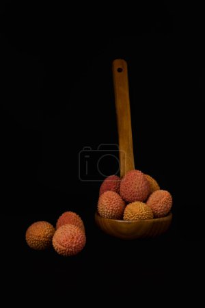 Téléchargez les photos : Fresh lychees in a wooden spoon isolated on a black background - en image libre de droit