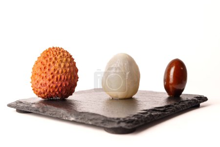 Foto de Whole fresh lychee, peeled and pitted on white background on a black tile - Imagen libre de derechos