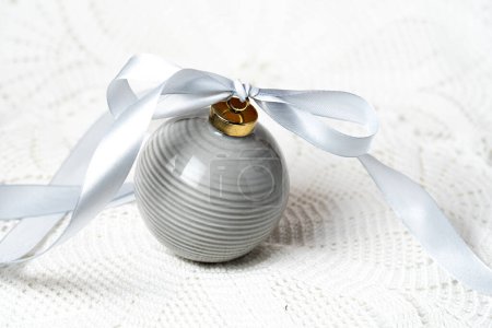 Photo for GRAY CERAMIC CHRISTMAS BALL WITH A GRAY RIBBON ON A LACE TABLECLOTH - Royalty Free Image