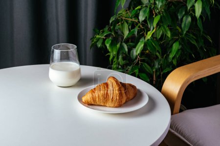 Foto de Milk in a glass and a croissant on a plate on a white table - Imagen libre de derechos