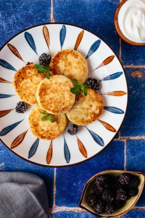 Téléchargez les photos : Cottage cheese pancakes on a plate, blackberries, sour cream. breakfast - en image libre de droit
