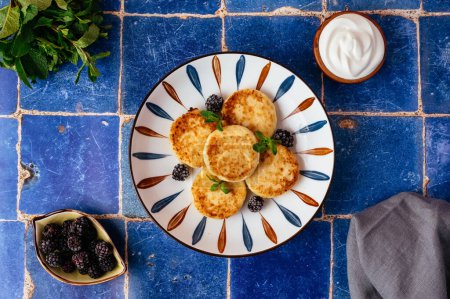 Téléchargez les photos : Cottage cheese pancakes on a plate, blackberries, sour cream. breakfast - en image libre de droit