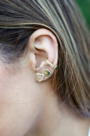 Téléchargez les photos : Femme portant des boucles d'oreilles. Boucles d'oreilles à l'oreille de la jeune femme, accessoires pour femmes, boucles d'oreilles en or - en image libre de droit