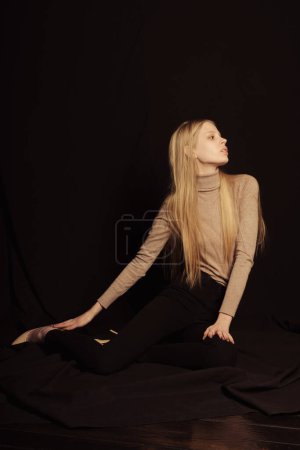 Photo for Portrait of a beautiful woman with long blonde hair blowing in a wind, wearing long black gothic costume. isolated against a black background. - Royalty Free Image