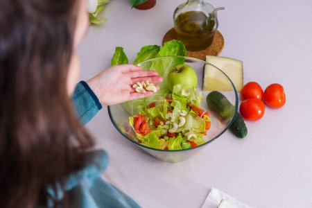 Téléchargez les photos : Woman adding cashews to a healthy salad at her kitchen table - en image libre de droit