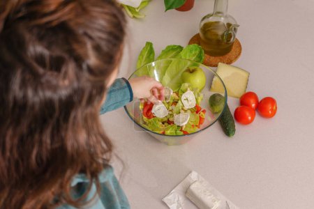 Téléchargez les photos : Above view of a woman adding goat cheese to a healthy salad at her kitchen table - en image libre de droit