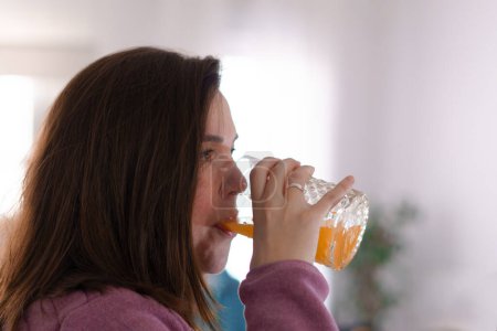 Téléchargez les photos : Close-up of a young brunette girl in profile drinking freshly squeezed orange juice - en image libre de droit