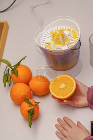 Photo for Woman's hands squeezing oranges in a juicer in her kitchen at home - Royalty Free Image
