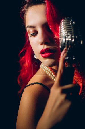 Photo for Gorgeous red haired woman singing with retro microphone on the stage - Royalty Free Image