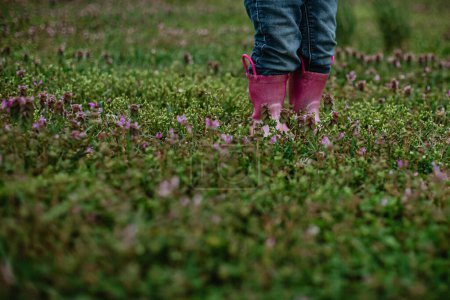 Foto de Niño pequeño de pie en flores silvestres en botas de lluvia brillantes - Imagen libre de derechos