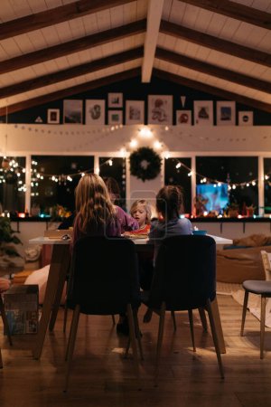 Foto de Familia sentada en una mesa por la noche rodeada de luz navideña - Imagen libre de derechos