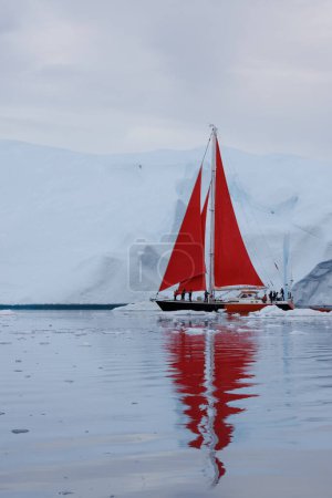 Foto de Sailboat with red sails sailing between huge icebergs - Imagen libre de derechos