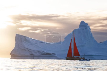 Téléchargez les photos : Sailboat with red sails sailing between huge icebergs - en image libre de droit