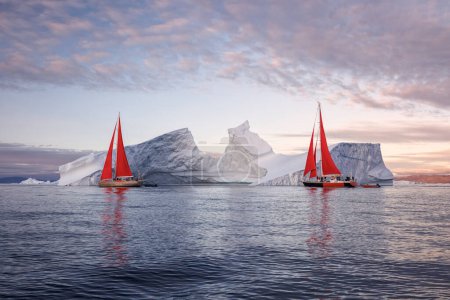 Foto de Sailboats with red sails sailing between huge icebergs - Imagen libre de derechos