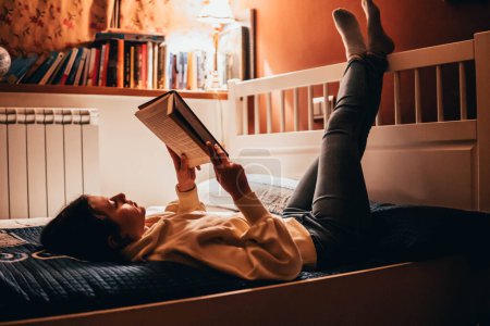 Photo for Woman reading a book lying in bed at night - Royalty Free Image