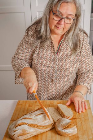 Téléchargez les photos : Woman cutting slices of freshly baked bread - en image libre de droit