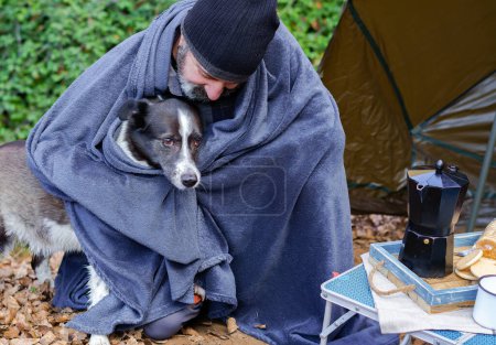 Téléchargez les photos : Man camping covered with a blanket with his dog - en image libre de droit