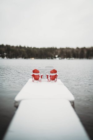 Photo for Red adirondack muskoka chairs on end of snowy dock in winter. - Royalty Free Image