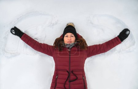 Téléchargez les photos : Top view of woman in red winter coat making snow angel on winter day. - en image libre de droit