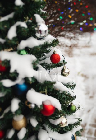 Foto de Snow covered evergreen tree decorated with Christmas balls outside. - Imagen libre de derechos