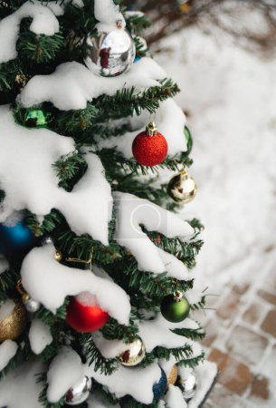 Foto de Snow covered evergreen tree decorated with Christmas balls outside. - Imagen libre de derechos
