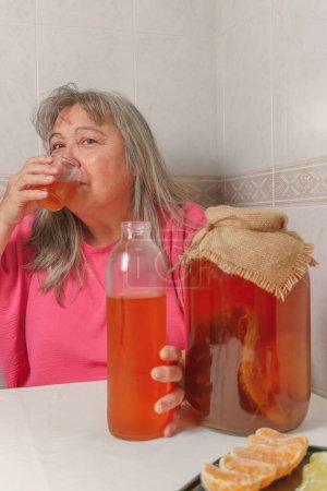 Téléchargez les photos : Elderly woman drinking a glass of fermented kombucha tea alternative health concept - en image libre de droit