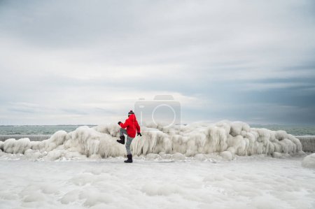 Téléchargez les photos : Child in red coat breaking ice on frozen pier on winter day. - en image libre de droit