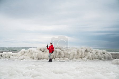 Photo for Boy in red coat holding icicle on frozen icy pier in winter. - Royalty Free Image