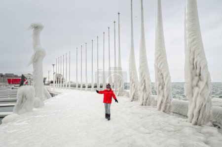 Téléchargez les photos : Child in red coat walking carefully on ice covered pier in winter. - en image libre de droit