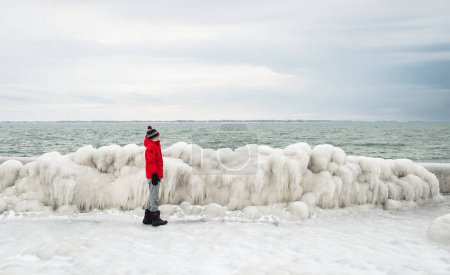 Photo for Child in red coat standing on ice covered frozen pier in winter. - Royalty Free Image