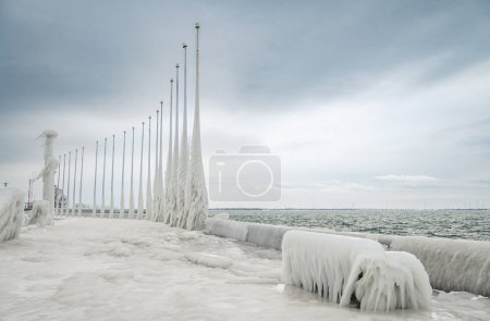 Téléchargez les photos : Ice covered bench on frozen lakeshore pier after a winter storm. - en image libre de droit
