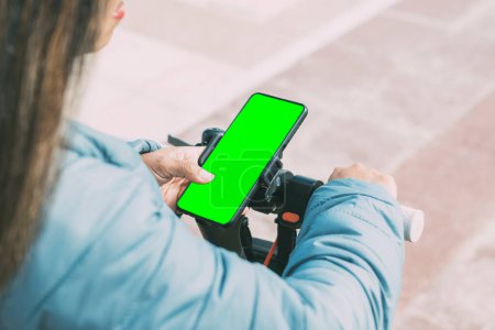 Foto de Beautiful latina woman, middle age 40-50 years old, long hair, uses smart phone application to unlock electric scooter, green screen, for apps. - Imagen libre de derechos