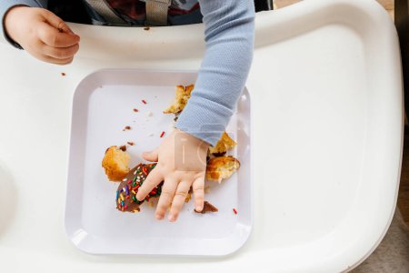Téléchargez les photos : Young Boy Eating Chocolate Sprinkle Donut in Highchair - en image libre de droit