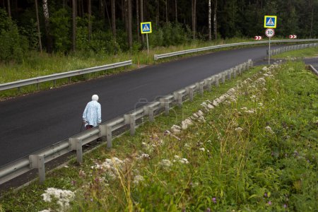 Téléchargez les photos : Old woman walks on empty highway. Woman on road. Pensioner walks outdoors - en image libre de droit