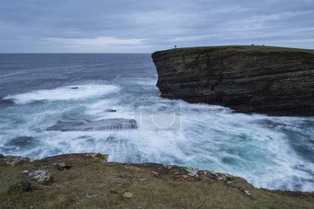 Téléchargez les photos : Photographer standing on cliffs above wild sea at Yesnaby, Orkney, Scotland - en image libre de droit