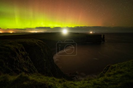 Photo for Northern lights shine in sky over sea cliffs and lighthouse at Duncansby head, Caithness, Scotland - Royalty Free Image