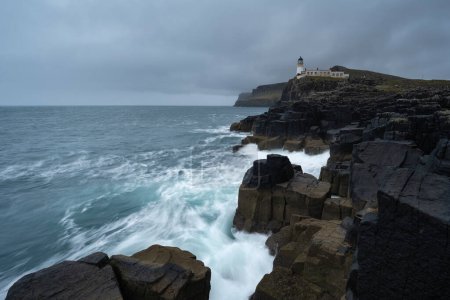 Téléchargez les photos : Neist Point lighthouse rises over rocky coastline, Isle of Skye, Scotland - en image libre de droit