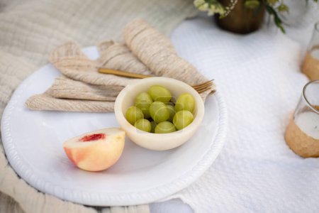 Photo for Plate of Green Grapes and a Peach on a Picnic Blanket - Royalty Free Image