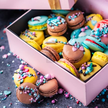 Photo for Pink box filled with macarons in brown and yellow with sprinkles - Royalty Free Image