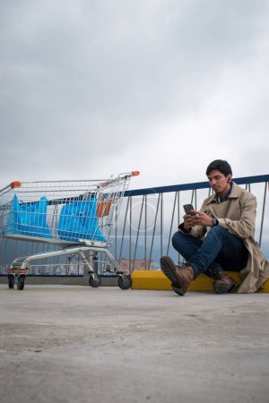 Foto de Mercado de coches y el hombre mirando su teléfono en un aparcamiento en día nublado - Imagen libre de derechos