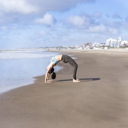 Photo for A woman practicing yoga on the water at the beach, doing Wheel (Urdhva Dhanurasana) pose. - Royalty Free Image