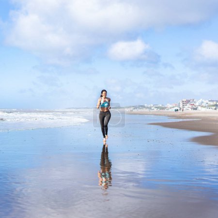 Téléchargez les photos : Woman running at the beach while reflected in the water - en image libre de droit
